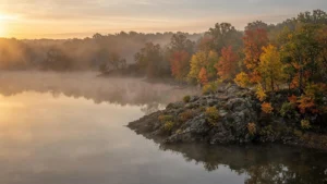 Mist rising off a calm reservoir lined with autumn trees on a cool fall morning