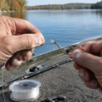 Close-up of an angler cinching a wet knot onto a worm hook on a boat deck beside line and weights.