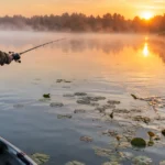 Best time to fish for bass: an angler casting a topwater lure near lily pads on a misty lake at sunrise