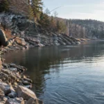 December bass fishing along a steep rocky bluff on a reservoir, with frost on the rocks and low winter sun